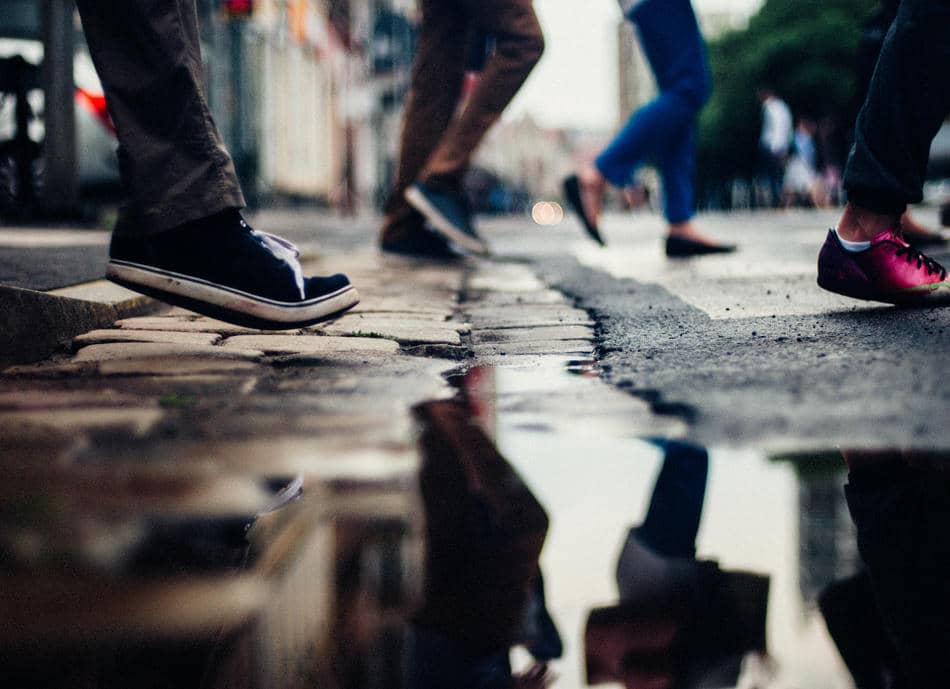 Blurred feet moving quickly across a city street with reflections in a puddle