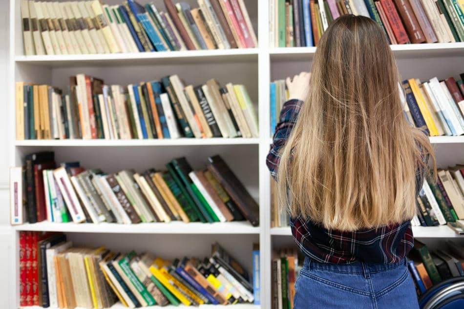 Person standing in front of a large bookshelf, representing the many small decisions that contribute to decision fatigue.