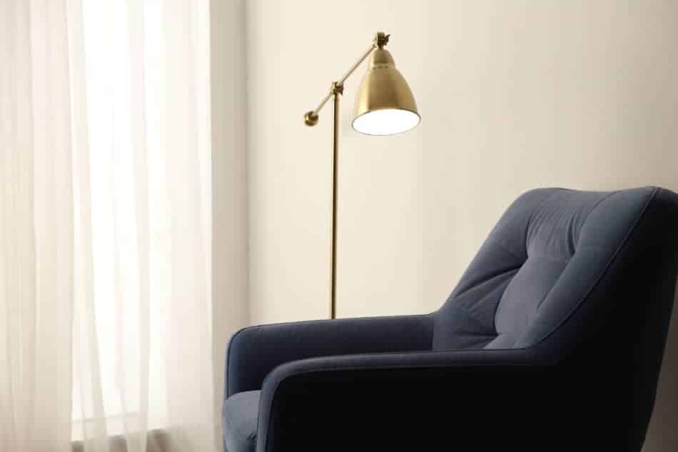 Empty blue armchair beside a window with sheer curtains and a floor lamp
