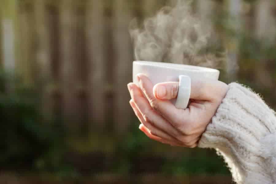 A person holding a warm cup with steam rising, representing a slow and intentional moment that helps reduce rushing and improve clarity.