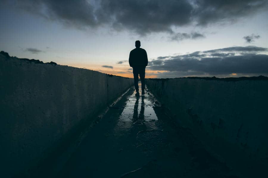 A person standing alone on a dark road under a cloudy sky, reflecting during a difficult moment