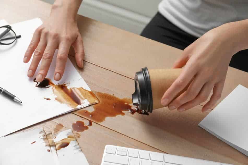 A person cleaning up spilled coffee on a desk after a small mishap