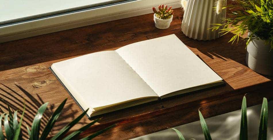 Open journal on a wooden desk beside a sunlit window with soft natural light