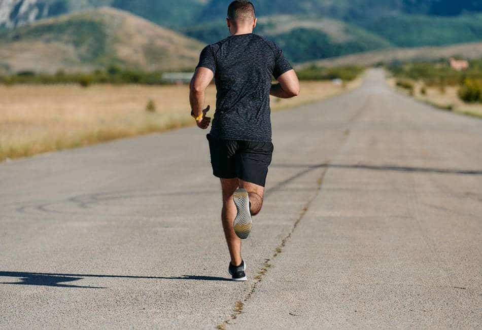 Runner moving down a long open road surrounded by a wide landscape.