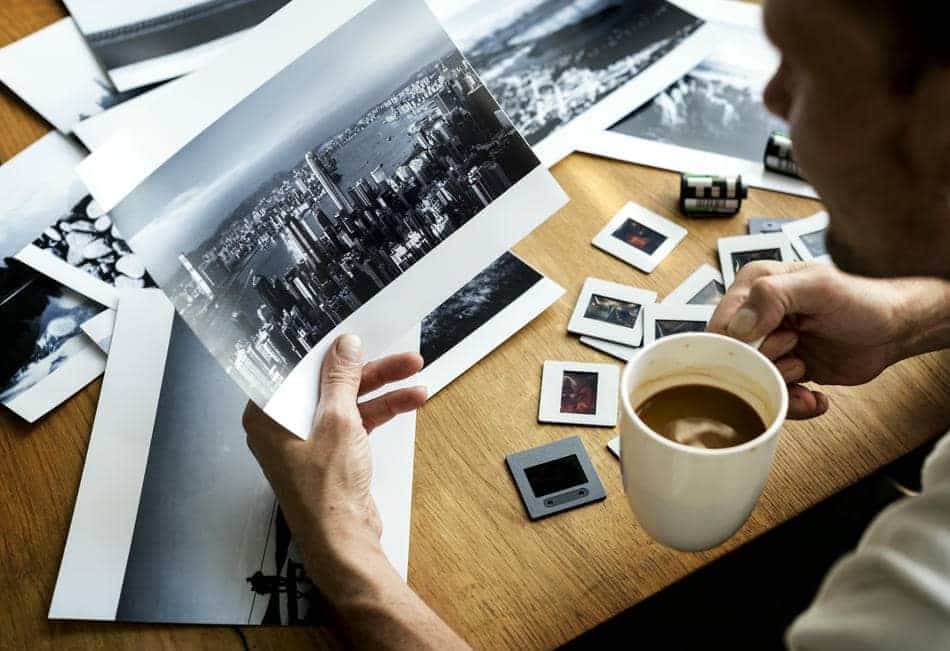 Person reviewing old photographs while sitting at a desk with a cup of coffee nearby.