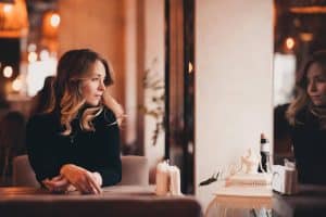 Thoughtful woman sitting in a café beside her reflection, quietly reflecting during a mid-year self-reflection moment.