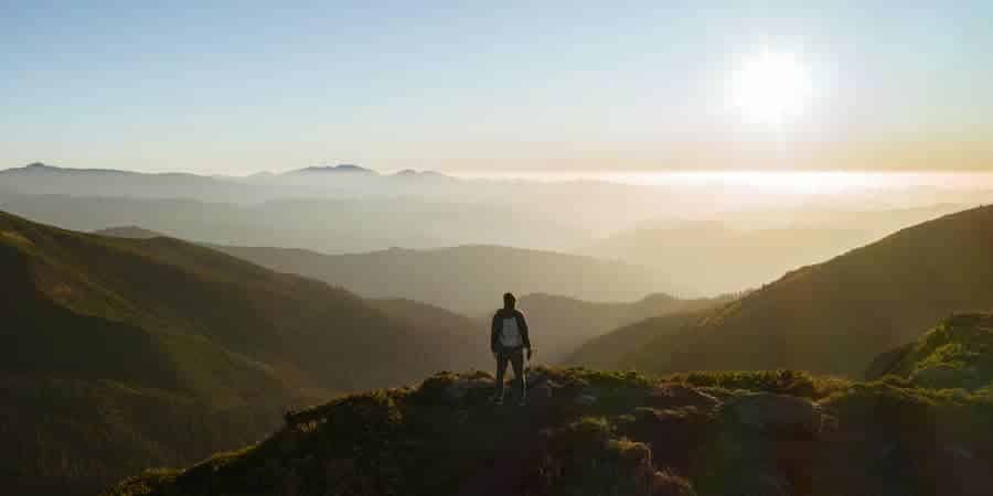 Person standing on a mountain ridge overlooking a vast landscape at sunrise, symbolizing gaining perspective and clarity through self-awareness.
