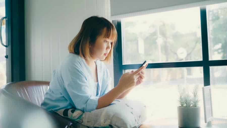 A person sitting by a window looking at their phone, representing how small moments of joy are often overlooked
