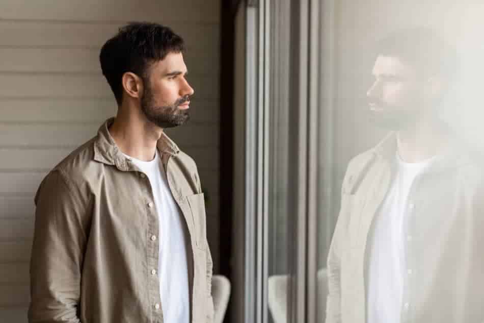 Thoughtful man standing beside his reflection in a window