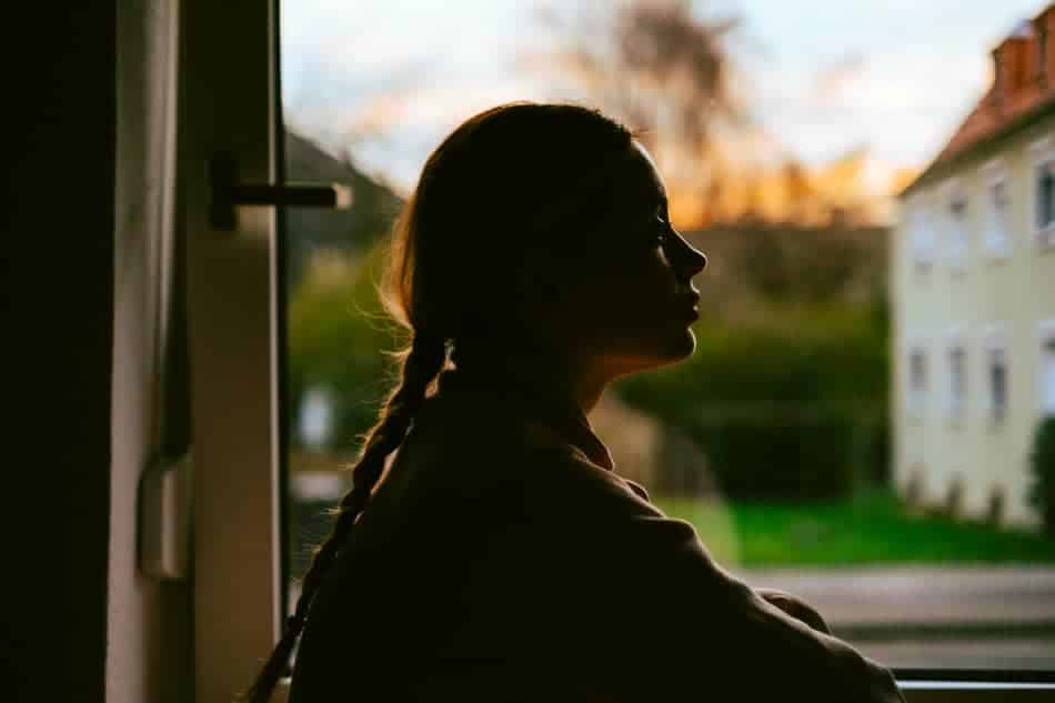 Person sitting by a window in silhouette, quietly reflecting in soft evening light