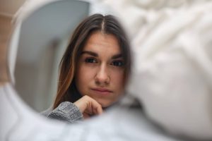 Young woman thoughtfully looking into a softly blurred mirror, symbolizing self-awareness, reflection, and self-compassion.