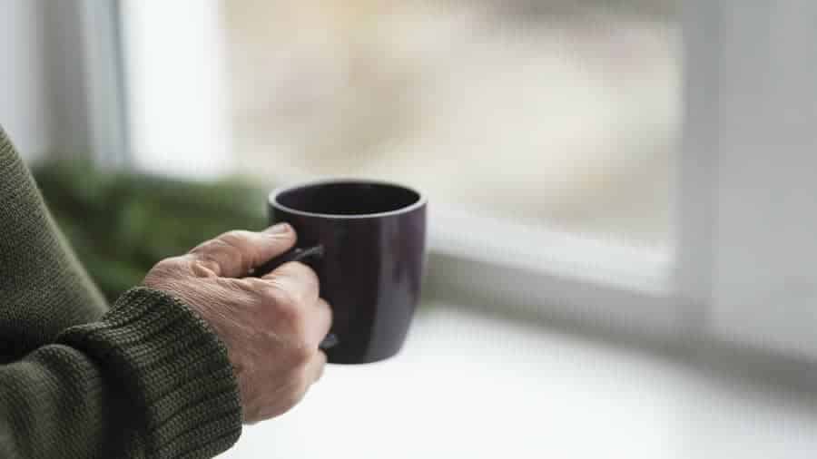 A person holding a warm mug by a window in soft natural light, representing small everyday joys