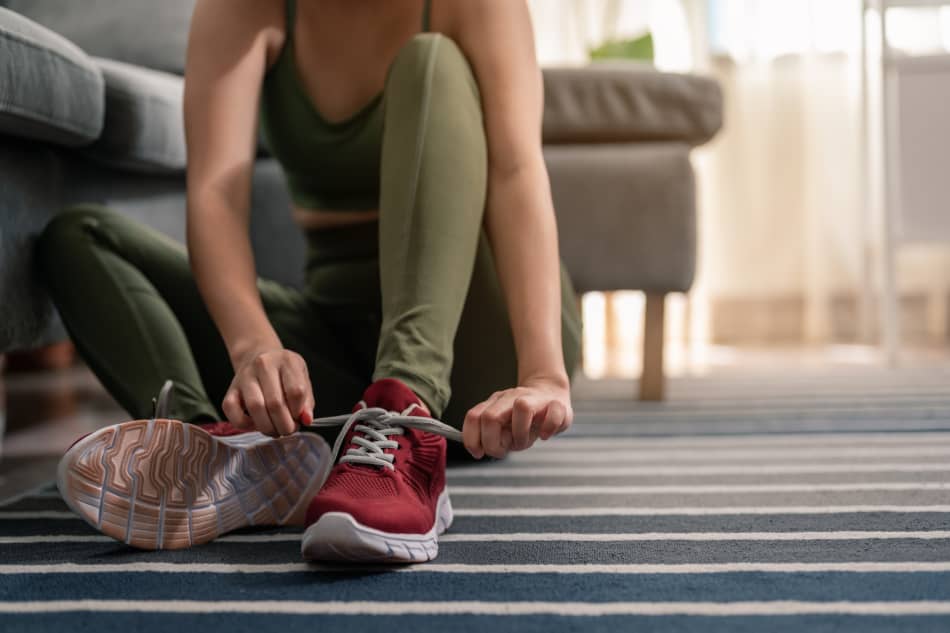 Woman sitting at home tying a pair of running shoes