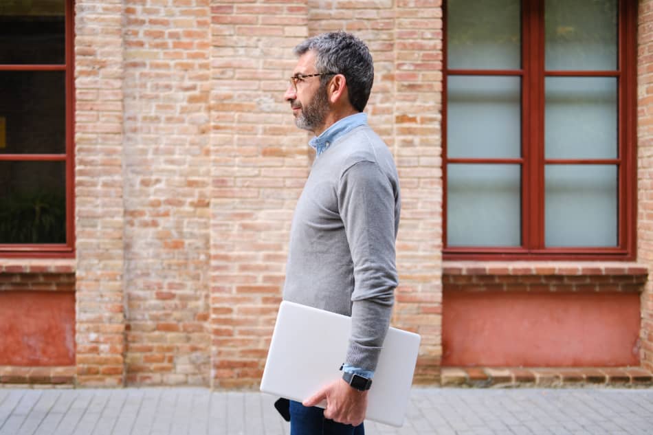 Man walking beside a brick building carrying papers in his hand