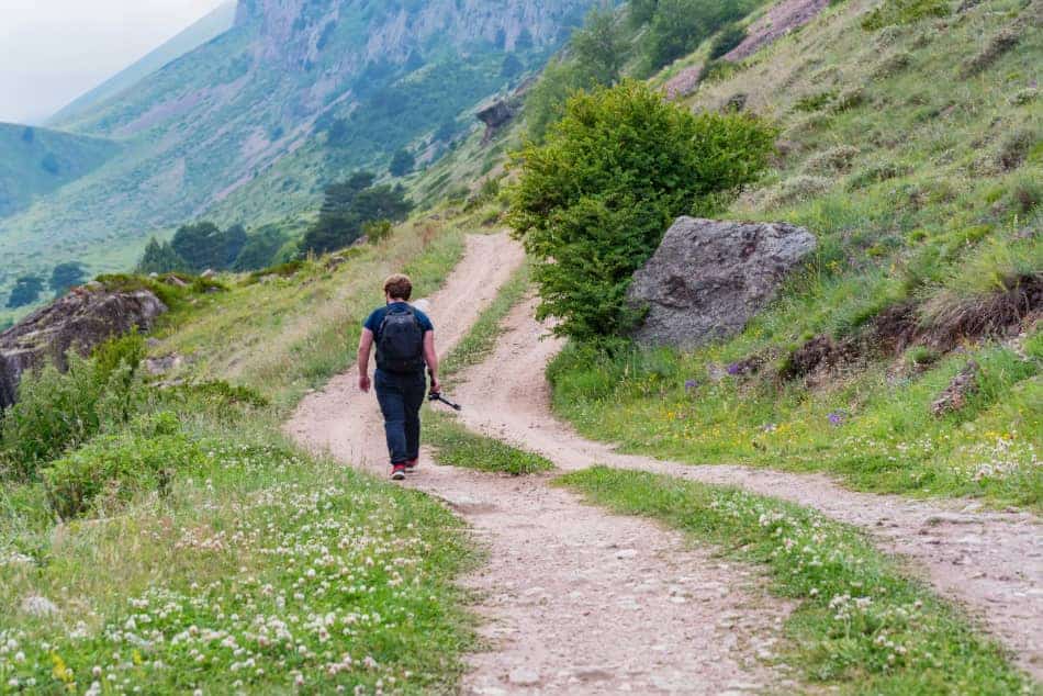 Person walking alone along a mountain path that branches ahead