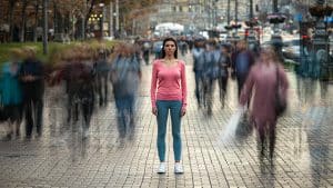 A person standing still in a busy city street while people move quickly around them in motion blur, representing why rushing makes you less productive.