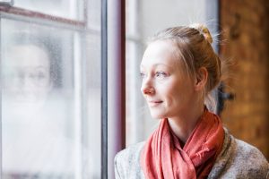 Woman quietly looking out a window while reflecting in a calm moment of presence.